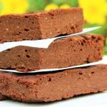 Três pedaços de brownie sobrepostos com flores amarelas ao fundo desfocadas