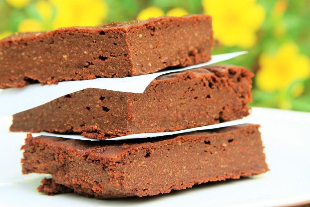 Três pedaços de brownie sobrepostos com flores amarelas ao fundo desfocadas