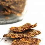 Três biscoitos quadrados amontoados sobre mesa branca, ao fundo o vidro com mais biscoitos desfocado