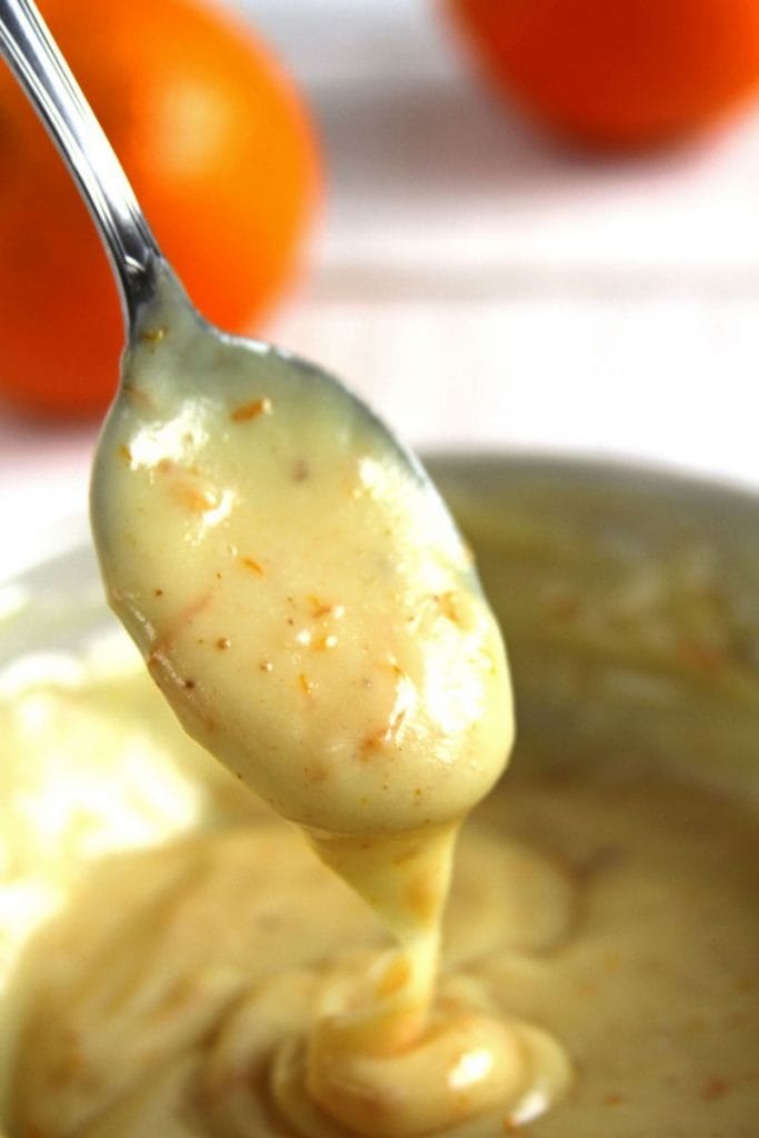 Brigadeiro branco com raspas de laranja em uma colher de metal sobre mesa branca