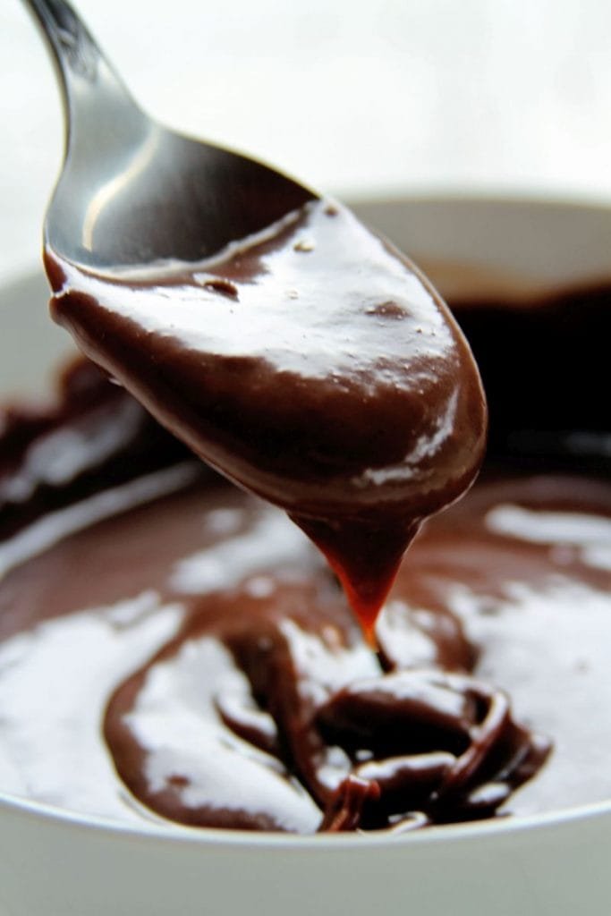 Brigadeiro preto em uma colher metálica sobre mesa branca