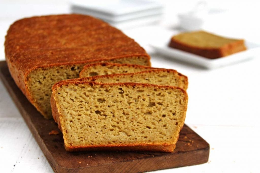 Pão de forma amarelo fatiado sobre tábua de madeira em mesa branca