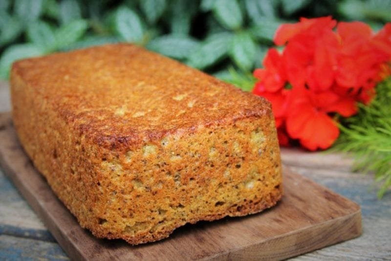 Pão de forma amarelo sobre mesa de madeira escura fundo verde e flor vermelha decorativa