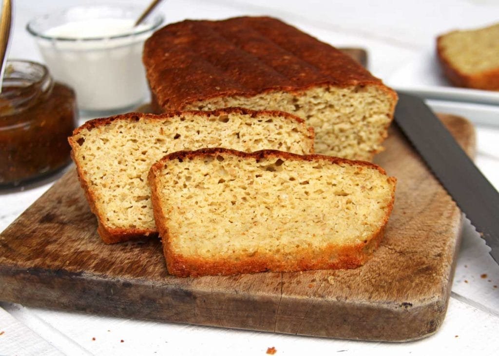 Pão de forma fatiado sobre tábua de madeira em uma mesa branca