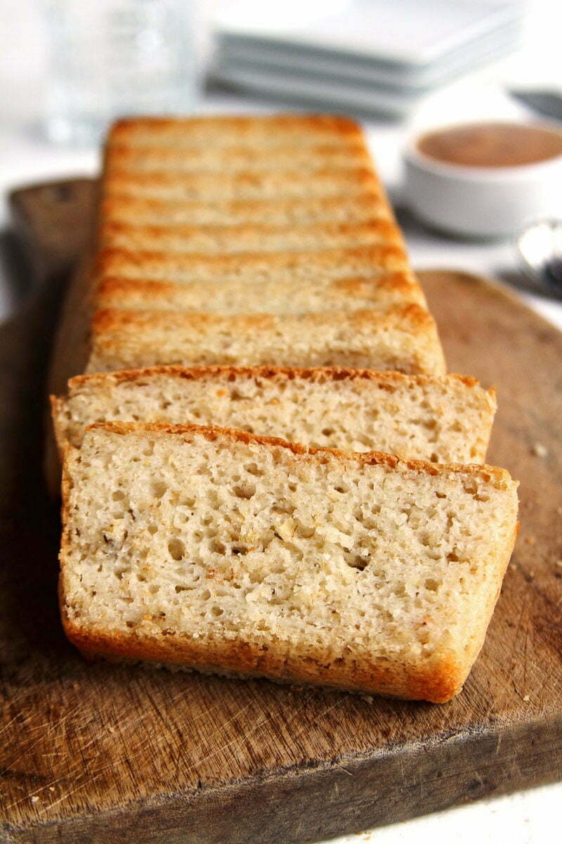 Pão de forma sem glúten fatiado sobre tábua de madeira em uma mesa branca