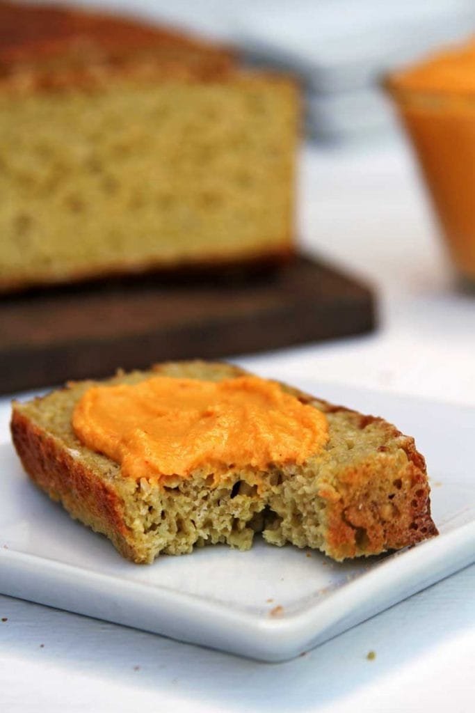 Fatia de pão mordida com patê amarelo por cima em um prato quadrado branco