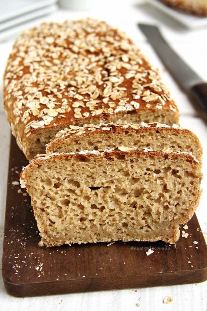 Pão de aveia fatiado na tábua de madeira sobre mesa branca