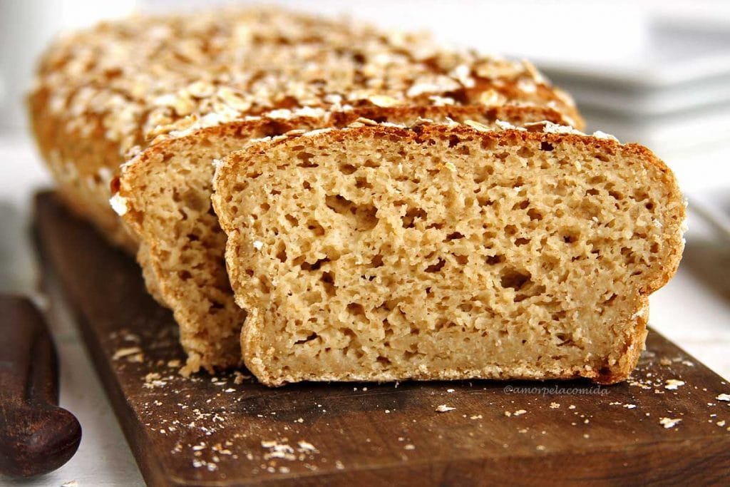 Pão de aveia fatiado na tábua de madeira sobre mesa branca