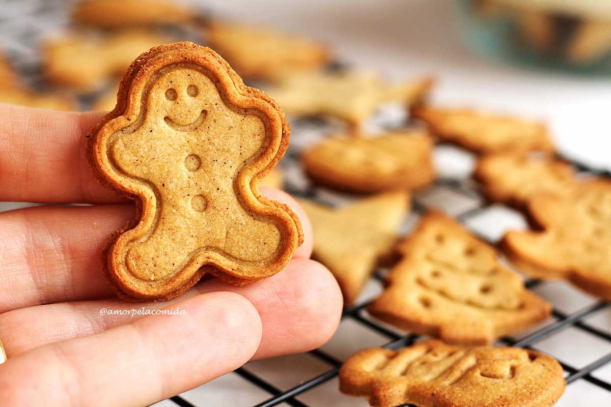 Mão segurando bolacha de natal em formato de boneco com biscoitos natalinos sobre uma grade preta de fundo