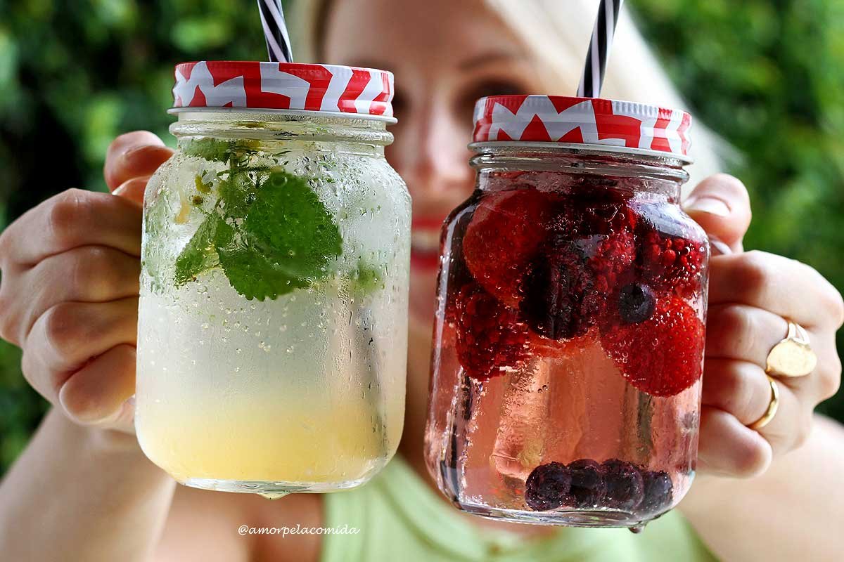 Dois copos de vidro com tampa vermelha e branca e canudo preto e branco com água com gás e frutas vermelhas