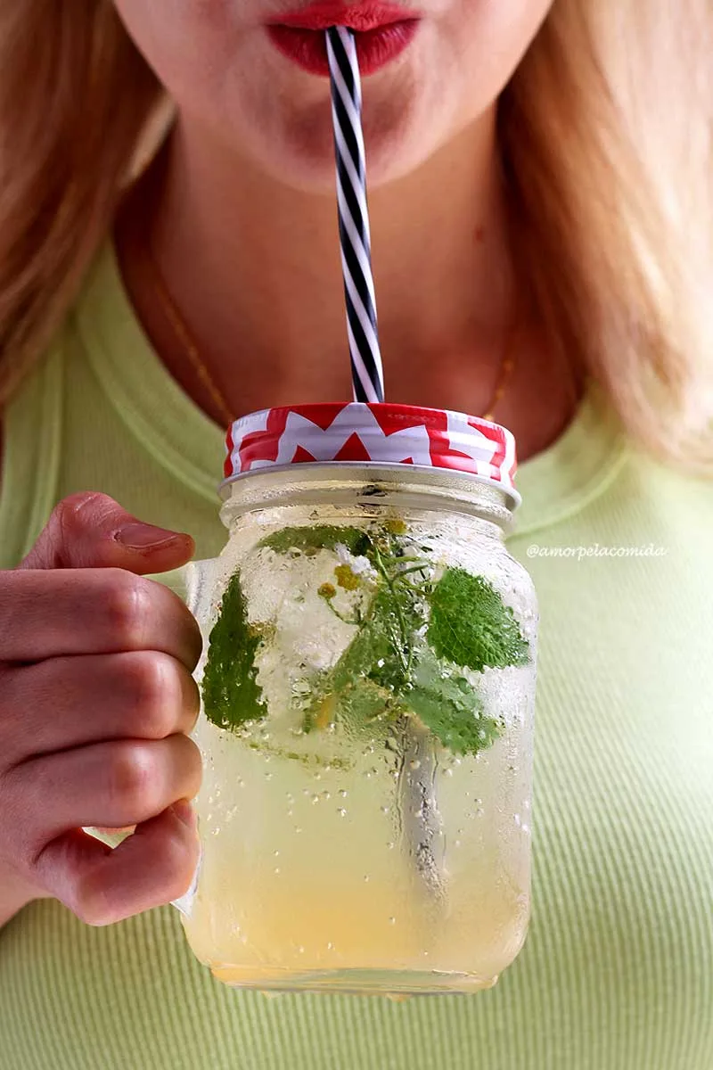 Woman holding glass of sparkling water with lemon and herbs