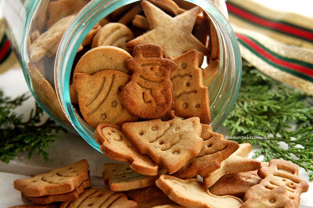 Biscoitos de natal saindo de dentro de vidro transparente com galhos verdes e fita decorando