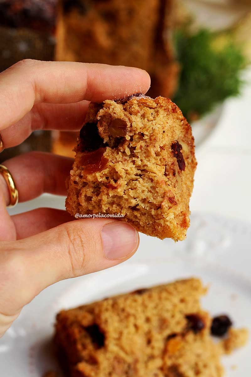 Mão segurando pedaço de panetone com frutas e gotas de chocolate