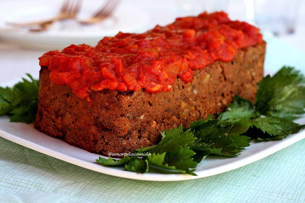 Bolo de carne vegetal coberto com molho de tomate sobre prato branco decorado com folhas de salsão