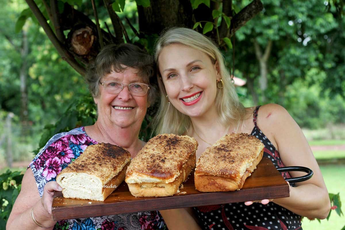 Duas mulheres segurando uma tábua com 3 cucas com farofa em cima em um jardim