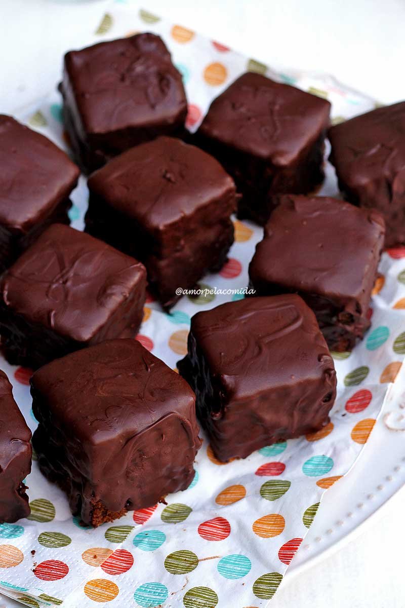 Vários pães de mel cobertos com chocolate sobre prato branco com guardanapo de bolinhas coloridas