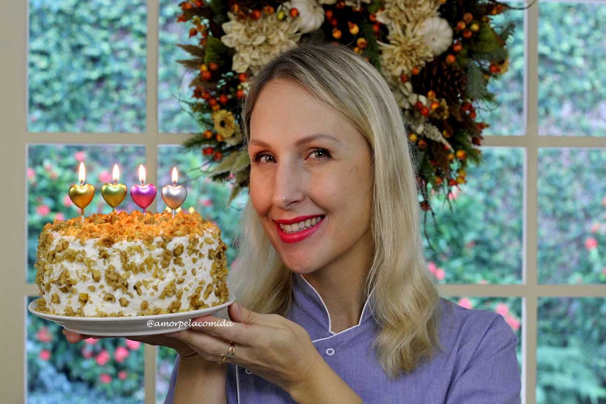 Mulher loira de uniforme azul segurando bolo de nozes com velas