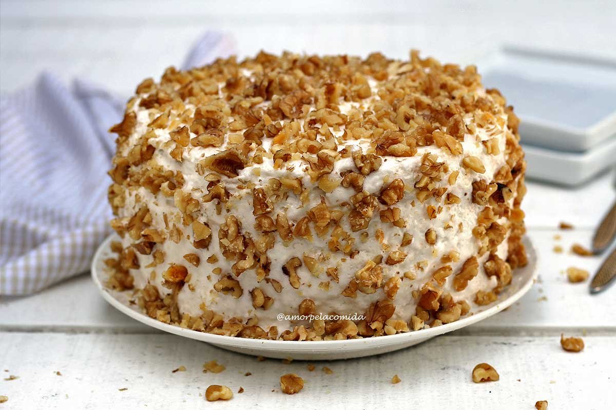 Bolo de nozes coberto com merengue suíço com nozes picadas sobre mesa branca