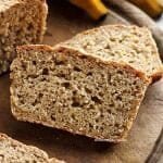 Duas fatias de pão de banana sobrepostas em uma tábua de madeira