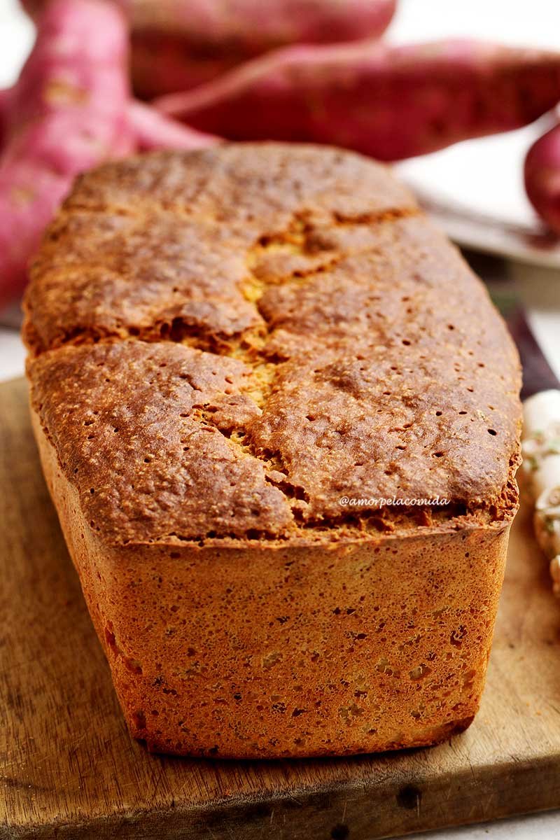 Pão de batata doce inteiro sobre tábua de madeira em mesa branca