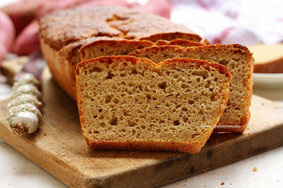 Pão de batata doce fatiado sobre tábua de madeira sobre mesa branca