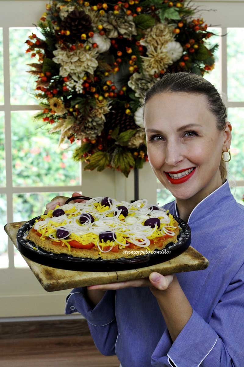 Mulher loira segurando tábua de madeira com forma de pizza