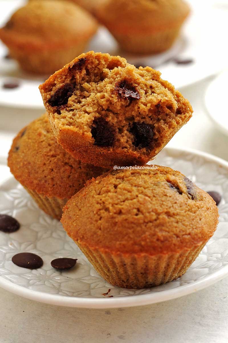 Um bolinho de baunilha com gotas de chocolate mordido sobre dois bolinhos inteiros em prato branco