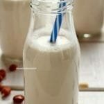 Glass bottle with peanut milk, blue and white striped straw on white table