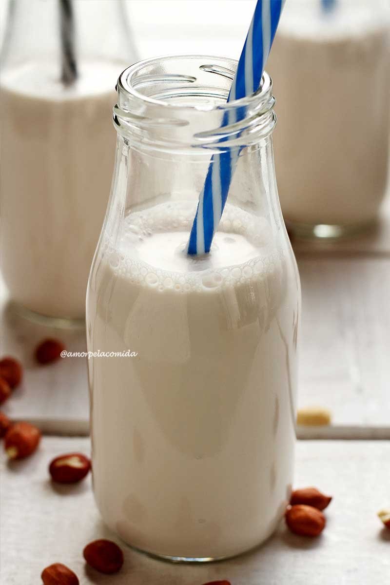 Glass bottle with peanut milk, blue and white striped straw on white table