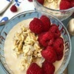 Two small bowls of oatmeal with raspberries on a blue table