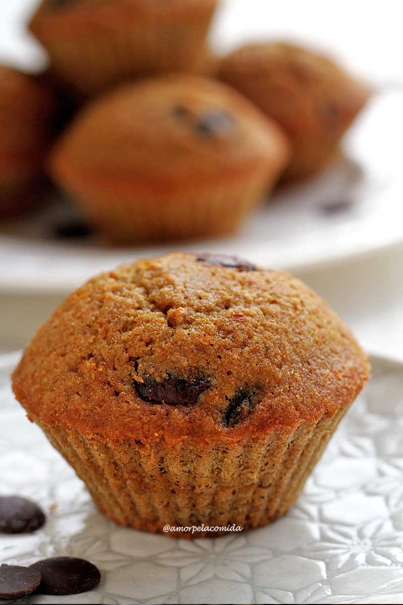 Bolinho pequeno de baunilha com gotas de chocolate sobre prato redondo branco em mesa branca, com mais bolinhos aos fundo