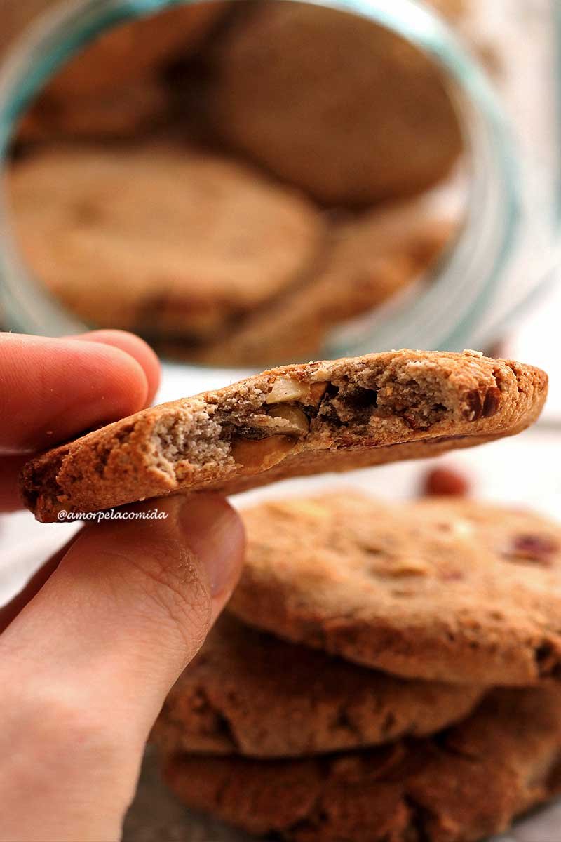 Mão segurando biscoito de amendoim sobre mesa branca com vários biscoitos