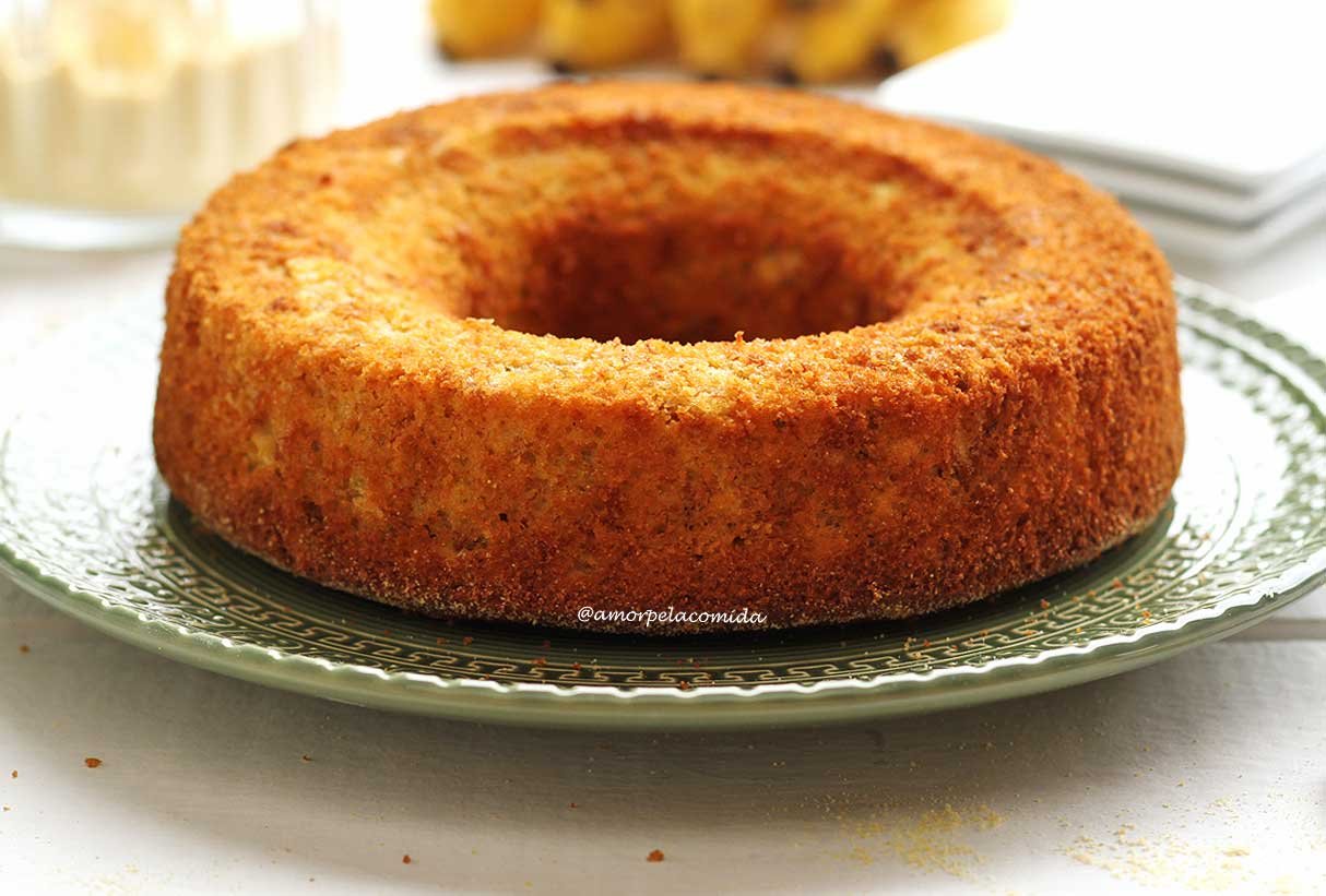 Bolo de fubá redondo com furo no meio sobre prato verde em uma mesa branca