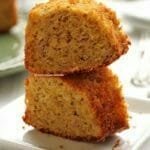 Duas fatias de bolo de fubá sobrepostas em um prato branco quadrado pequeno em mesa branca