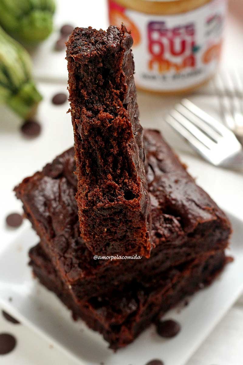 Três pedaços de brownie empilhados sobre prato branco, o pedaço de cima está em pé com duas mordicas