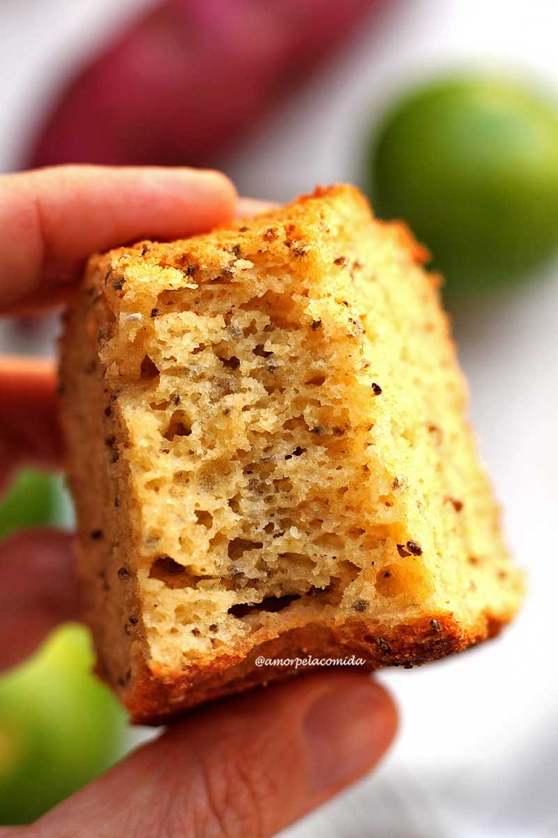 Mão segurando pedaço de bolo de limão mordido com limões e batata-doce ao fundo