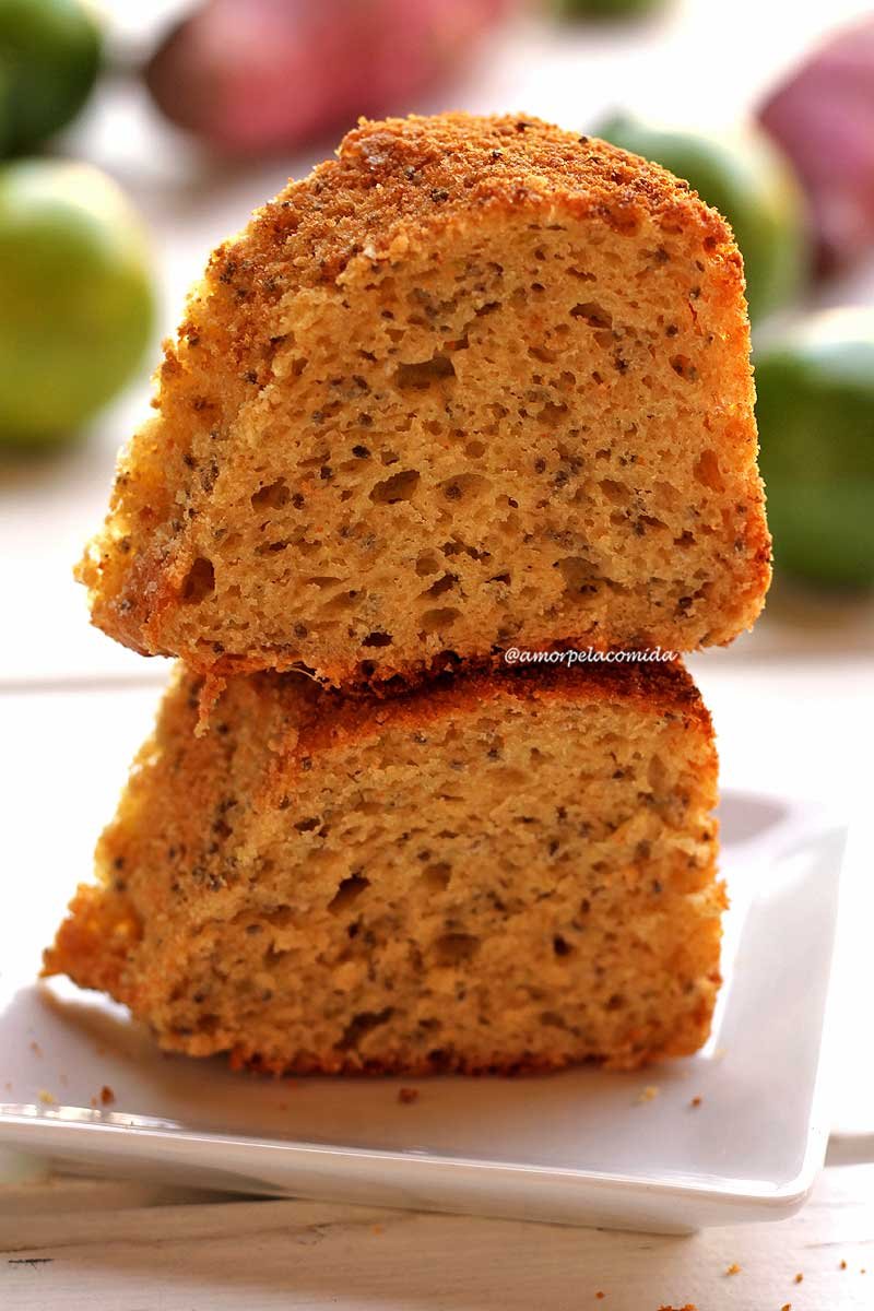 Duas fatias de bolo de limão sobrepostas em um prato quadrado pequeno sobre mesa branca com limões aos fundo