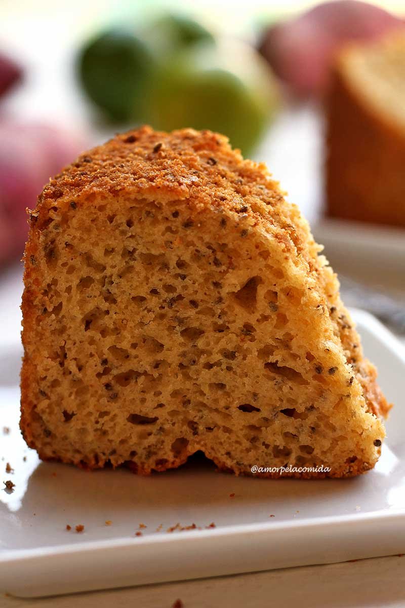 Pedaço de bolo de limão sobre prato branco quadrado pequeno em uma mesa branca com limão e batata-doce ao fundo