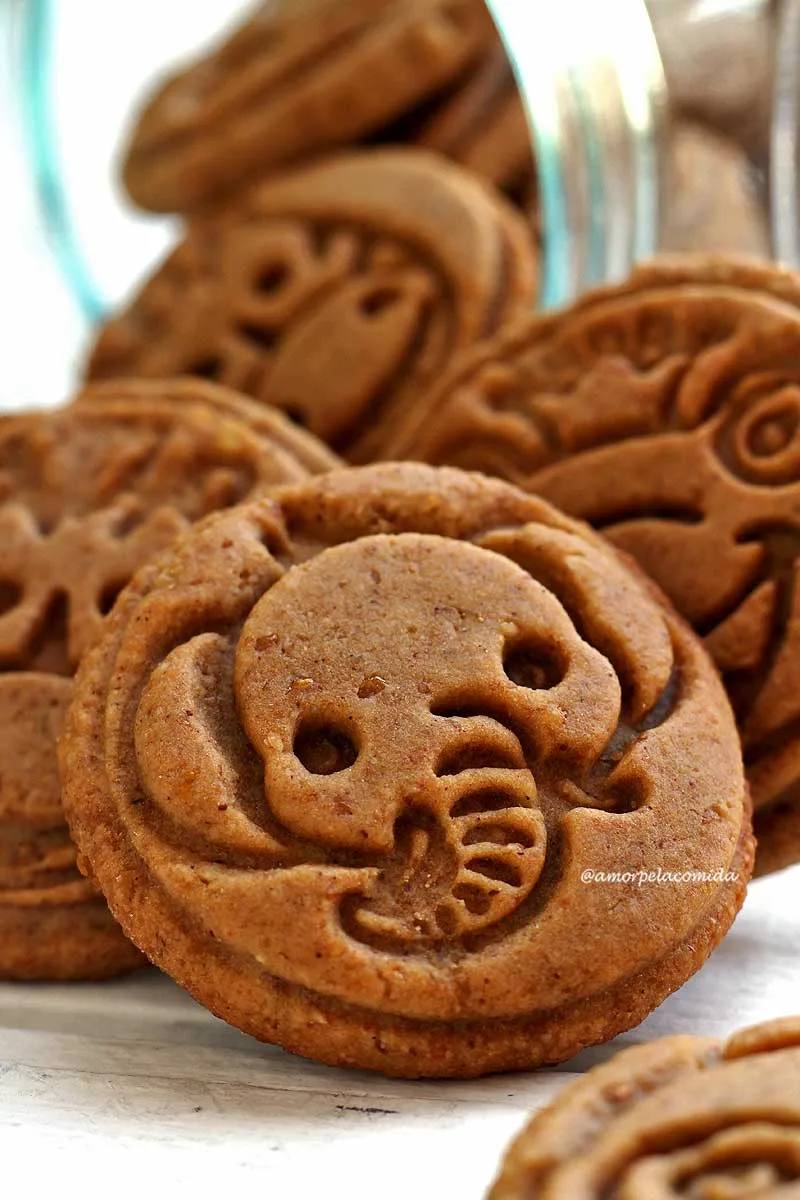 Vários biscoitos redondos saindo do vidro que está deitado sobre a mesa, o biscoito da frente tem carinha de elefante