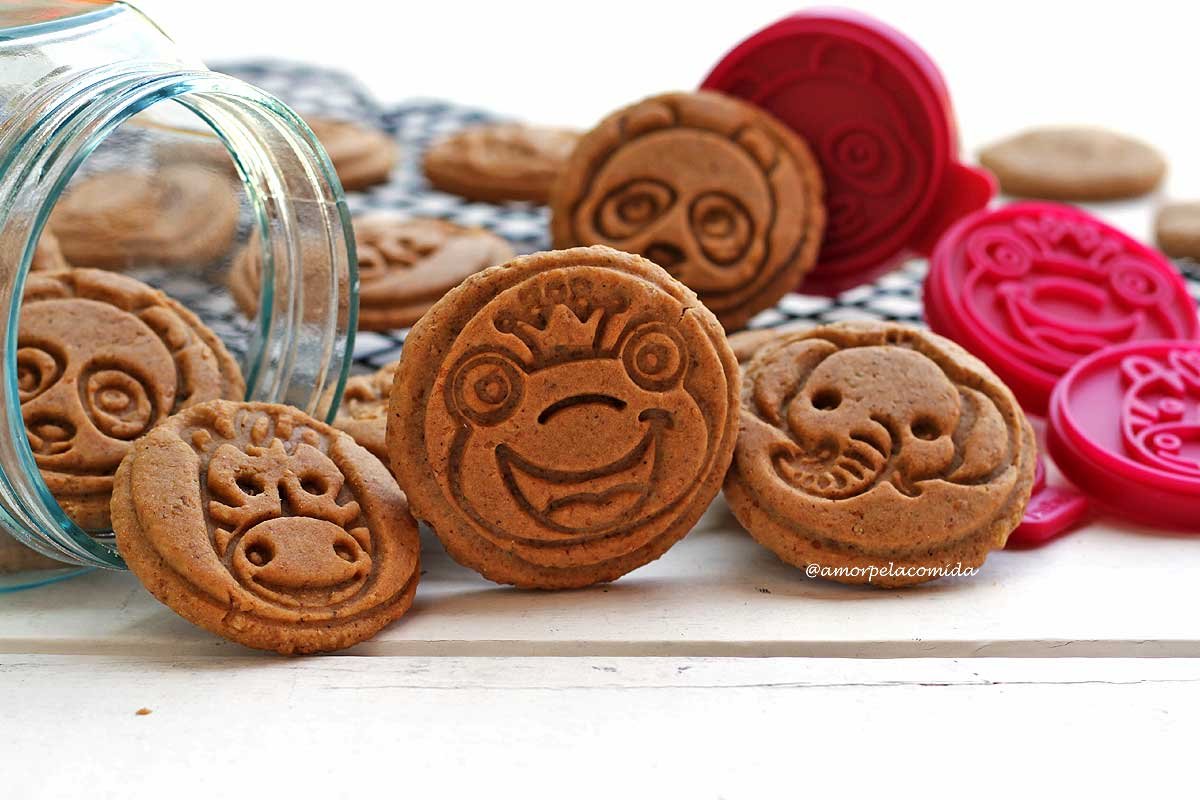 Several cookies coming out of a glass lying on a white table, the cookies have faces of frogs, zebras, elephants and pandas