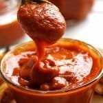 Small round glass jar with thick red sauce, with spoonful of sauce to better show the texture