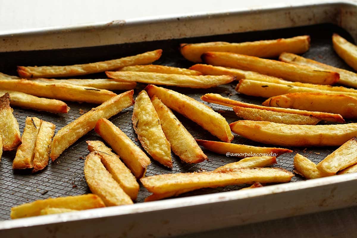 Vários toletes de batata assados em uma forma de metal grande sobre um tapete de silicone verde escuro