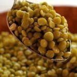 Colher cheia de ervilha cozida sobre bacia de bambu, dentro da bacia mais grãos de ervilha cozidos