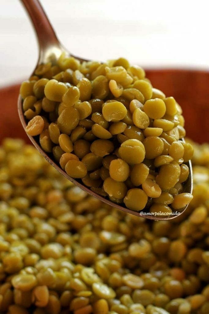 Cuillère pleine de petits pois cuits sur une bassine en bambou, à l'intérieur de la bassine plus de grains de pois cuits