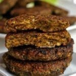 Dois hambúrgueres sobrepostos em um prato pequeno branco, sobre os hambúrgueres inteiros tem duas metade de um hambúrguer partido para mostrar a textura interna