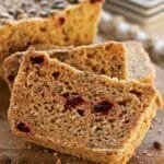 Três fatias de pão apoiadas umas nas outras em uma tábua de madeira, a fatia tem pedacinhos de cramberries e sementes dentro da massa