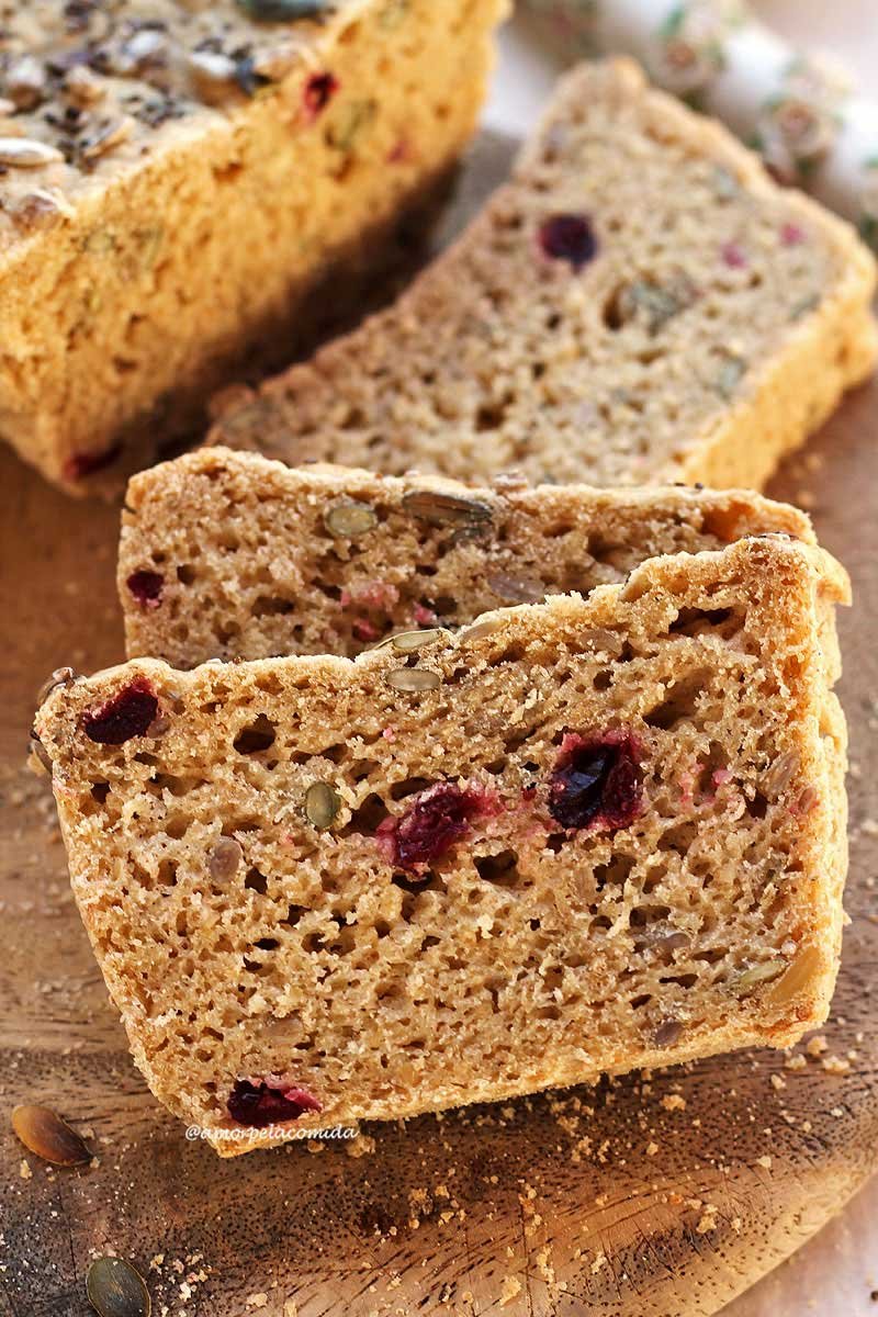 Três fatias de pão apoiadas umas nas outras em uma tábua de madeira, a fatia tem pedacinhos de cramberries e sementes dentro da massa