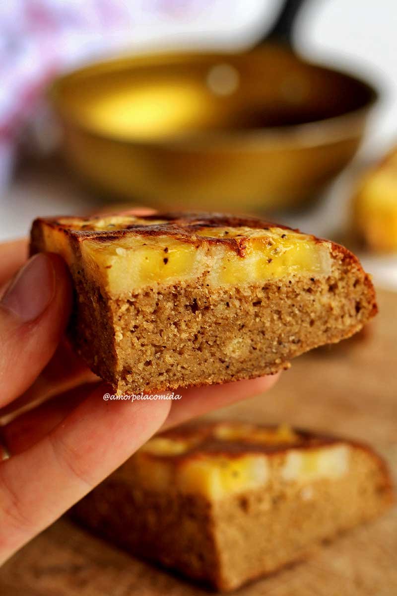 Mão segurando um pedaço de bolo de banana com fatias de banana por cima