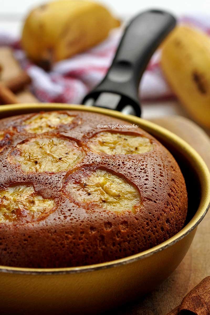 Frigideira dourada com bolo de banana dentro, no topo do bolo rodelas de banana