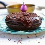 Bolo de chocolate redondo pequeno sobre prato azul turquesa, ao fundo uma frigideira amarela desfocada